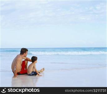 Side profile of a mid adult man and his son sitting on the beach, Bermuda