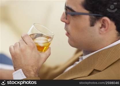 Side profile of a mid adult man drinking a glass of whiskey