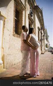 Side profile of a mid adult man embracing a pregnant young woman from behind, Santo Domingo, Dominican Republic