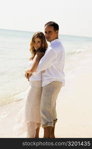 Side profile of a mid adult man embracing a young woman from behind on the beach