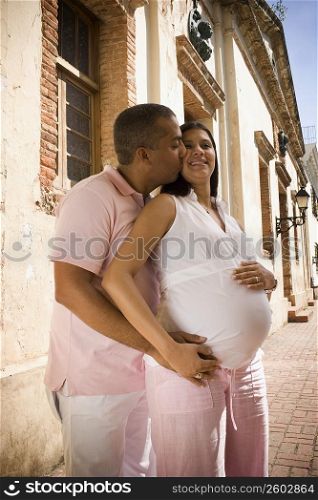 Side profile of a mid adult man embracing and kissing a pregnant young woman from behind, Santo Domingo, Dominican Republic