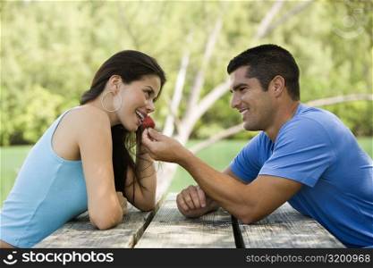 Side profile of a mid adult man feeding a young woman a strawberry