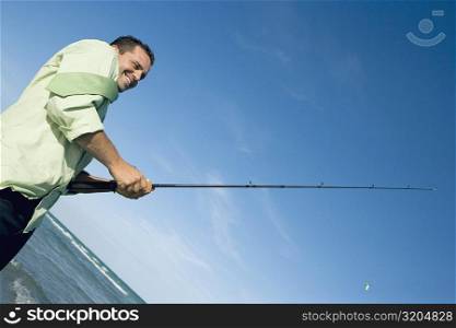 Side profile of a mid adult man holding a fishing rod on the beach