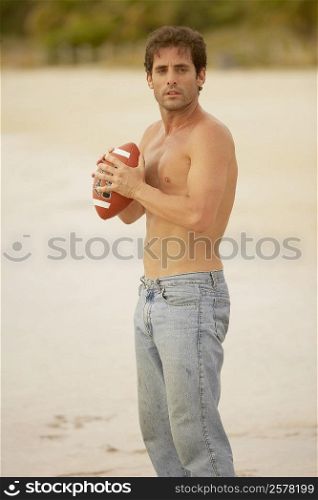 Side profile of a mid adult man holding a rugby ball on the beach