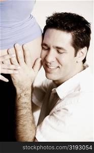 Side profile of a mid adult man listening to a pregnant young woman&acute;s abdomen and smiling