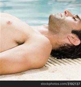 Side profile of a mid adult man lying at the edge of a swimming pool