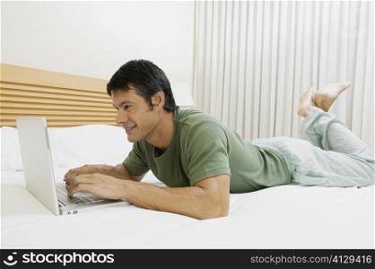Side profile of a mid adult man lying on the bed and using a laptop