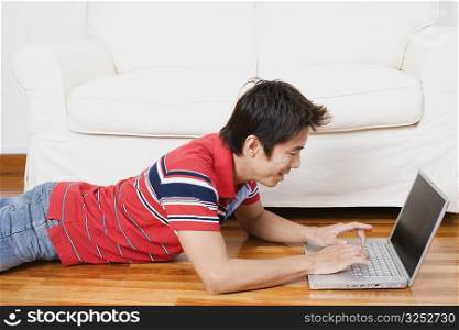 Side profile of a mid adult man lying on the floor and using a laptop