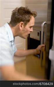 Side profile of a mid adult man opening a refrigerator door