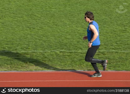 Side profile of a mid adult man running on a running track