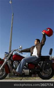Side profile of a mid adult man sitting on a motorcycle and raising his helmet