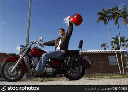 Side profile of a mid adult man sitting on a motorcycle and raising his helmet
