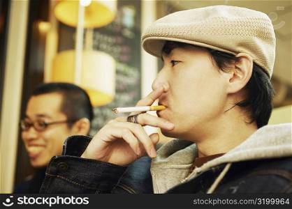 Side profile of a mid adult man smoking a cigarette and a young man smiling beside him