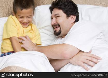 Side profile of a mid adult man tickling his son on the bed