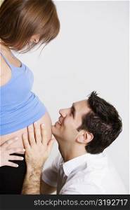 Side profile of a mid adult man touching abdomen of a pregnant young woman and smiling