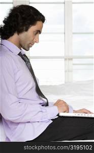 Side profile of a mid adult man using a laptop