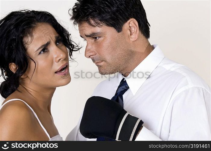 Side profile of a mid adult man wearing boxing gloves standing in front of a young woman