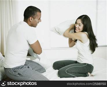Side profile of a mid adult man with a young woman having a pillow fight on the bed