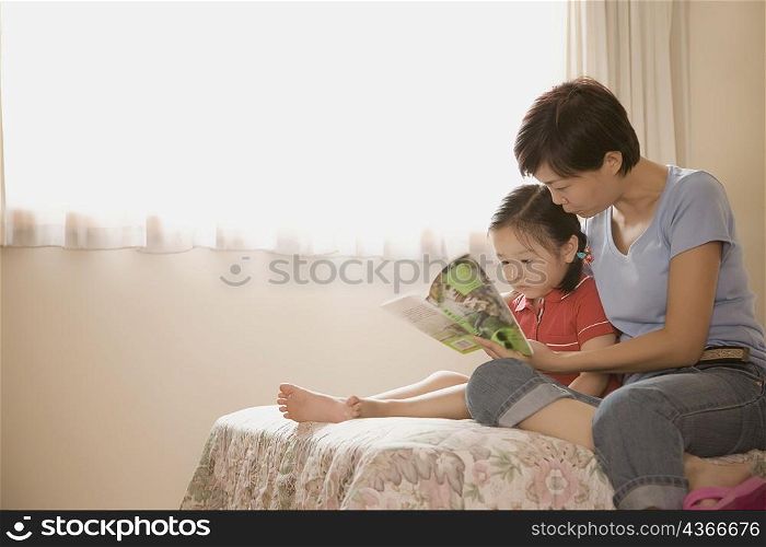 Side profile of a mid adult woman and her daughter reading a book