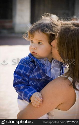 Side profile of a mid adult woman carrying and kissing her son