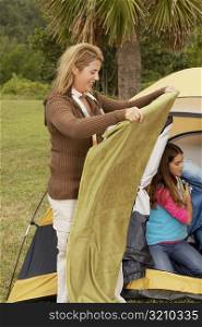 Side profile of a mid adult woman holding a blanket with her daughter near a tent