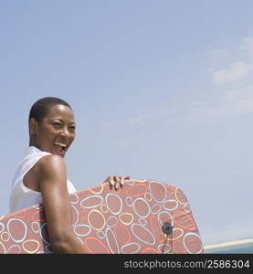 Side profile of a mid adult woman holding a body board and laughing