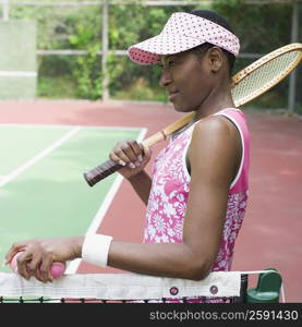 Side profile of a mid adult woman holding a tennis racket and tennis balls