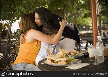 Side profile of a mid adult woman hugging and kissing her friend in a restaurant, Santo Domingo, Dominican Republic