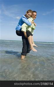 Side profile of a mid adult woman riding piggyback on a mid adult man on the beach