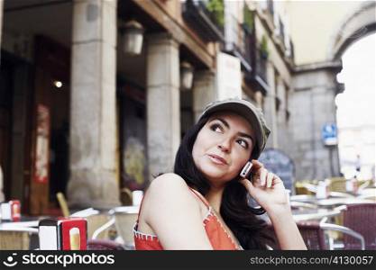 Side profile of a mid adult woman sitting at a sidewalk cafe and talking on a mobile phone