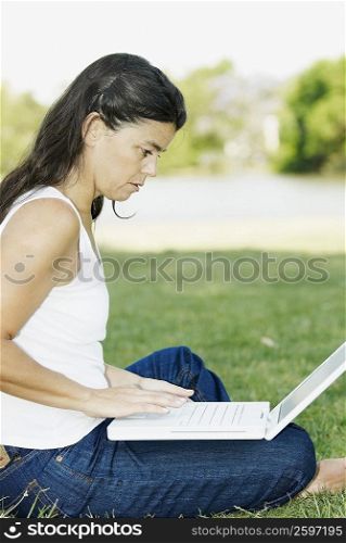 Side profile of a mid adult woman sitting in a park and using a laptop