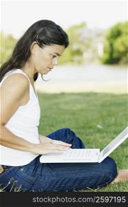 Side profile of a mid adult woman sitting in a park and using a laptop