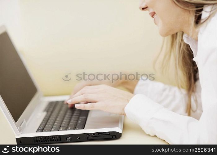 Side profile of a mid adult woman using a laptop and smiling