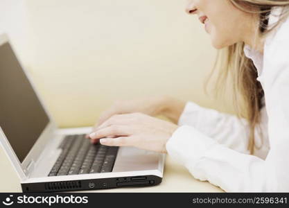 Side profile of a mid adult woman using a laptop and smiling