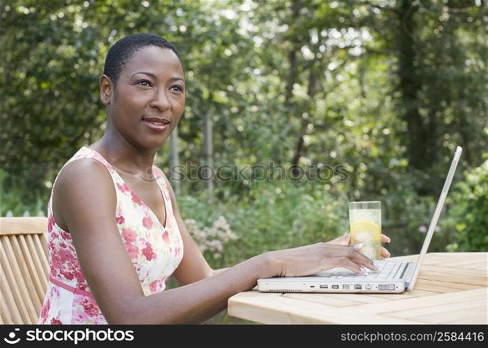Side profile of a mid adult woman working on a laptop and holding a glass of lemonade