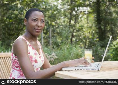 Side profile of a mid adult woman working on a laptop and holding a glass of lemonade