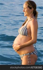 Side profile of a pregnant woman touching her abdomen