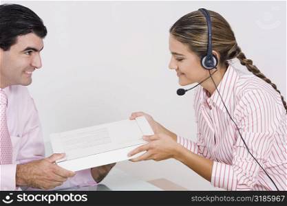 Side profile of a receptionist wearing a headset and receiving a box from a businessman