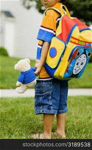 Side profile of a schoolboy carrying a schoolbag and a teddy bear
