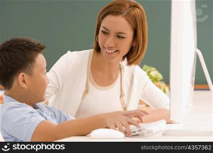 Side profile of a schoolboy with his teacher in front of a computer and smiling