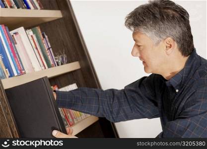 Side profile of a senior man picking a book from a bookshelf