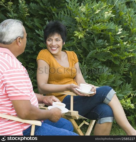 Side profile of a senior man sitting with a mature woman and holding cups of tea