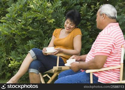 Side profile of a senior man sitting with a mature woman and holding cups of tea