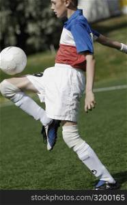 Side profile of a soccer player balancing a soccer ball on his thighs