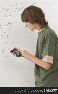 Side profile of a teenage boy calculating algebra equation in a calculator