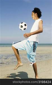 Side profile of a teenage boy playing with a soccer ball on the beach