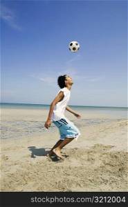 Side profile of a teenage boy playing with a soccer ball on the beach