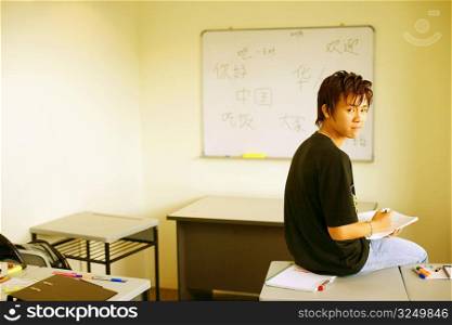Side profile of a teenage boy sitting on a desk in a classroom