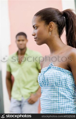 Side profile of a teenage girl looking sideways with a young man standing behind her