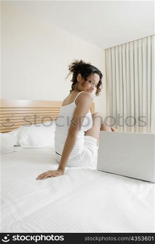 Side profile of a teenage girl sitting on the bed beside a laptop